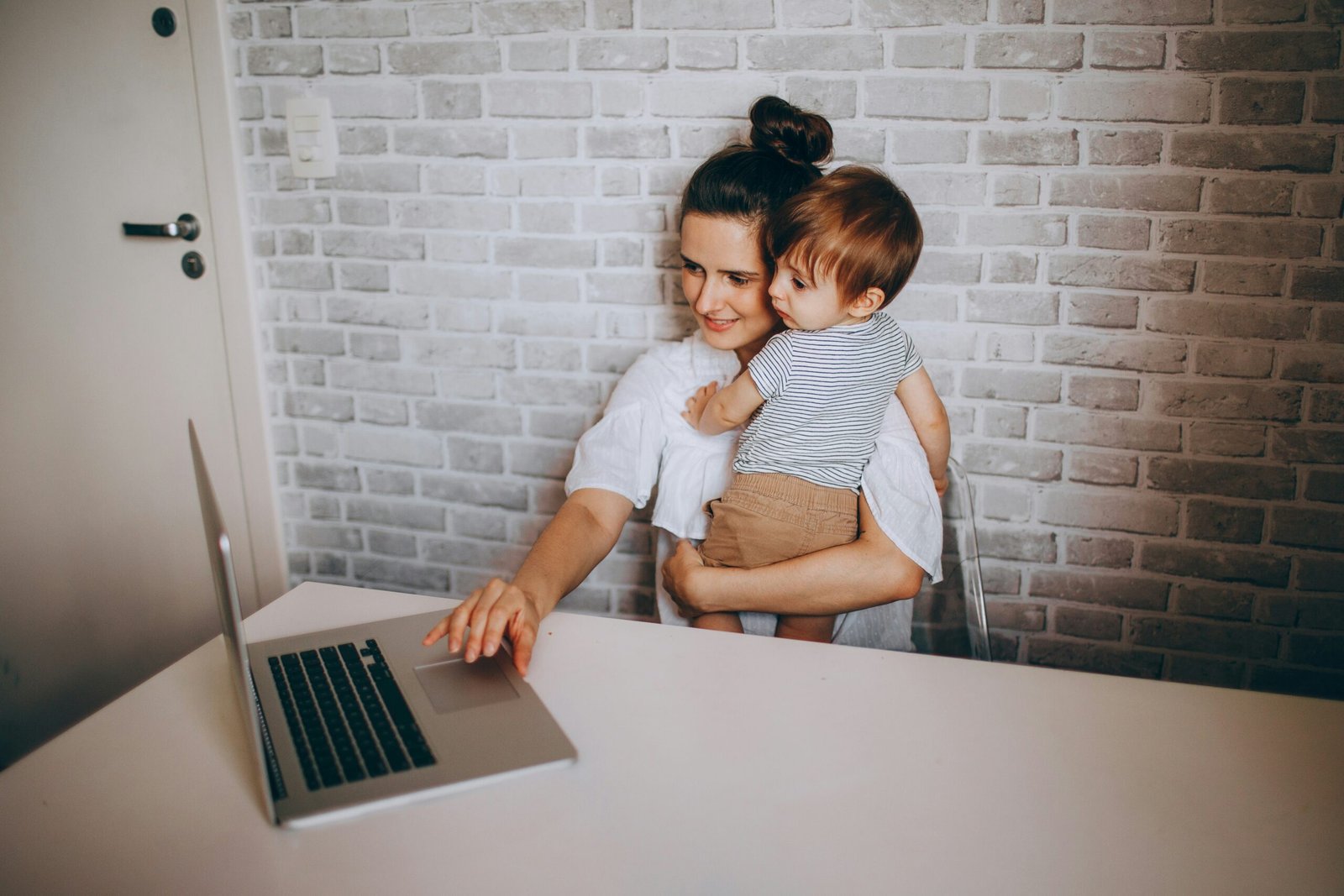 Mother holding her young child while using a laptop at home